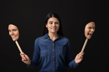 Woman holding masks with her face showing different emotions on black background. Balanced...