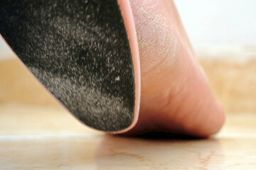 Woman using foot file for removing dead skin from feet at home, woman scrubbing foot process by...