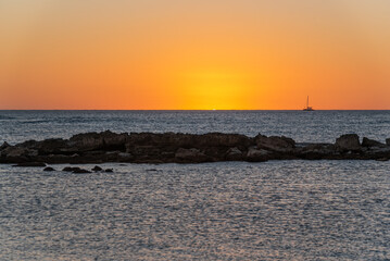 Orange sunset over ocean and reef with boat on horizon