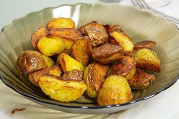A glass bowl of fried potatoes. Potatoes are cut into small pieces and are seasoned with herbs