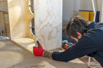 Middle aged Hispanic carpenter man working standing in his carpentry shop assembling a piece of furniture