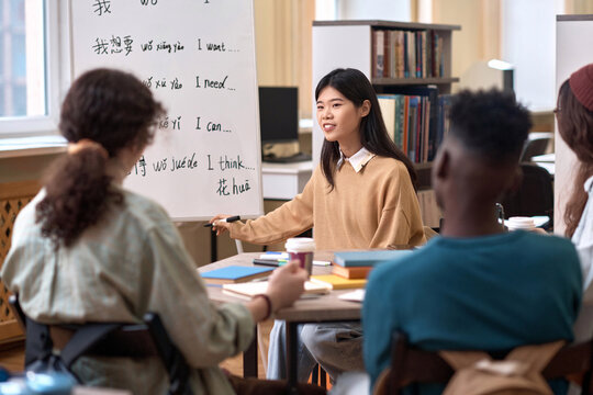 Portrait of smiling Asian female teacher explaining Chinese language grammar to students in library copy space