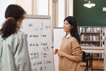 Portrait of friendly Asian woman teaching Chinese language to student standing by whiteboard in...