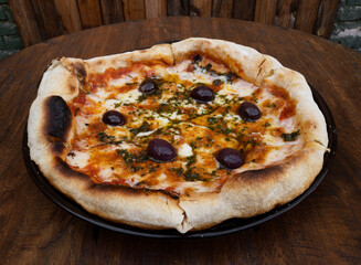 Traditional pizza. Top view of a mozzarella cheese pizza with tomato sauce, black olives and fresh oregano, on the wooden table.	
