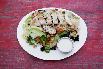 Caesar salad with rustic presentation. Top view of a fresh salad with lettuce, parmesan cheese, bread croutons, sliced grilled chicken breast, bacon and Caesar dressing.	
