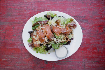 Caesar salad. Top view of fresh a Caesar salad with lettuce, parmesan cheese, bread croutons, smoked salmon, bacon and Caesar dressing, in a white dish on the restaurant table.