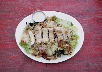 Caesar salad with rustic presentation. Top view of a fresh salad with lettuce, parmesan cheese, bread croutons, sliced grilled chicken breast, bacon and Caesar dressing.	
