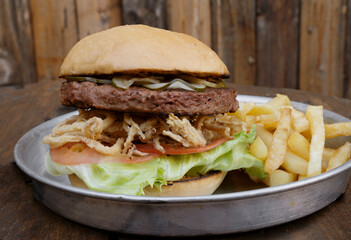 Vegetarian cuisine. Plant based burger. Not Burger. Closeup view of NotCo hamburger with tomato, lettuce, crispy onion rings and NotCo mayo, in a metal dish on the restaurant wooden table.	
