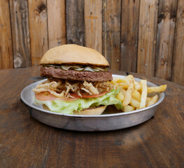 Vegetarian cuisine. Plant based burger. Not Burger. Closeup view of NotCo hamburger with tomato, lettuce, crispy onion rings and NotCo mayo, in a metal dish on the restaurant wooden table.	
