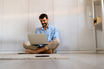 Male sitting on floor uses Internet, writes project report. Productive distant worker from home. - 761680107