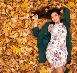 Autumn portrait of a young beautiful woman lying on fallen leaves
