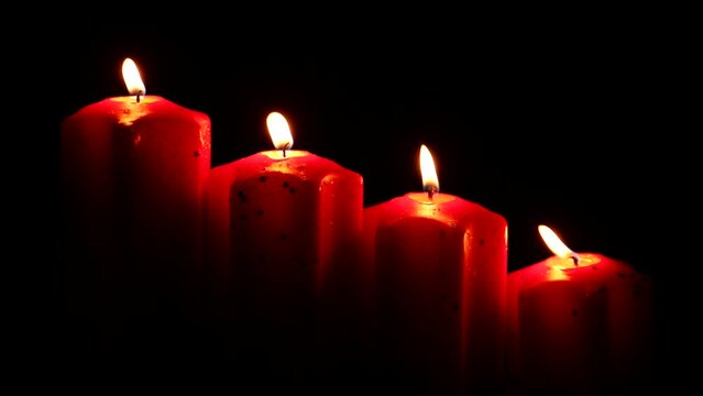 candele rosse su sfondo nero accese con fiamme oro e gialle che evocano un'atmosfera incantevole suggestiva religiosa e natalizia quasi mistica
