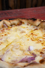 Traditional fugazzeta pizza background. Closeup view of a pizza with onion, red onion, mozzarella cheese and garlic, in a pizza pan on the red wooden table.	