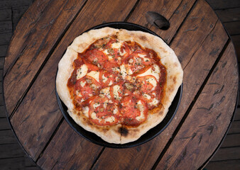 Top view of a traditional Neapolitan pizza with mozzarella cheese, roasted garlic, sliced tomatoes and fresh oregano leaves, on the restaurant wooden table.	
