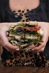 Dining in the restaurant. Closeup view of a woman holding a sliced multilayer vegetarian sandwich with fresh arugula, sun dried tomatoes, brie cheese and mushrooms.	
