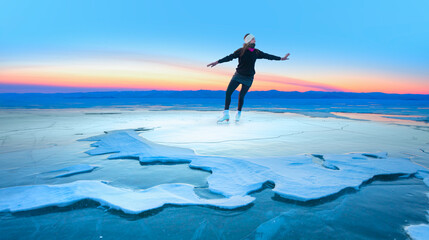 Fototapeta na wymiar A young happy woman is skating on the transparent ice of the frozen Lake Baikal on a sunny winter day - World-famous figure skater 