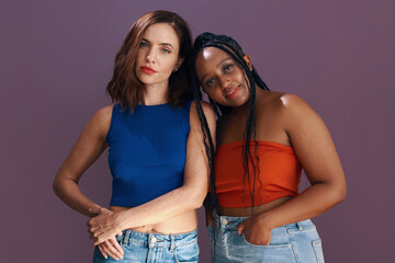 Best friends in tops and jeans posing against purple background