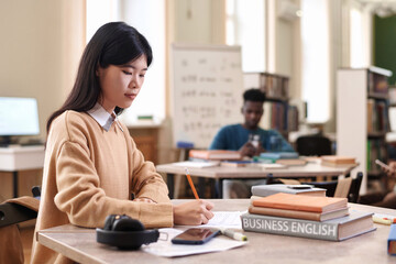 Side view portrait of young intelligent Asian woman studying business english in college library...