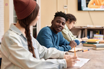 Portrait of African American young man smiling at friend during group study or college class copy space