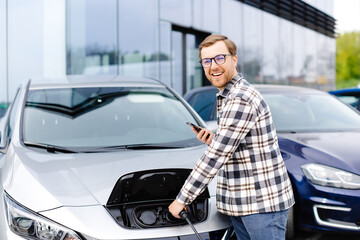 Young man plugging charging cable into the car socket. Electric car charging concept