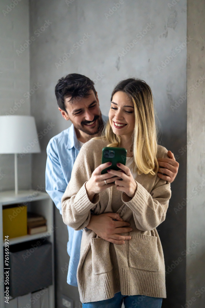 Wall mural Happy young couple, woman and man hugging, using smartphone together. Social media concept.