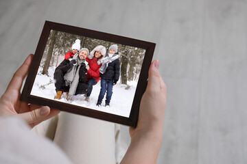 Woman holding frame with photo portrait of her family indoors, closeup