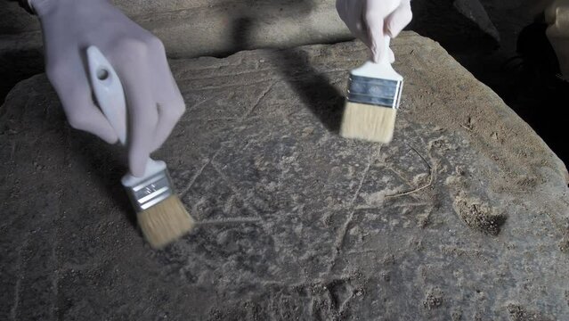 Close-up of two archaeologists' hands using brushes to remove dust and dirt from a Star of David carved into a stone tombstone. Ancient Jewish burial and symbol of Israel. Israeli territory