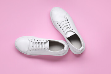 Pair of stylish white sneakers on pink background, top view