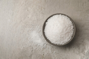 Natural salt in bowl on grey textured table, top view. Space for text