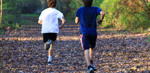 Two boys running fast on a trail covered in leaves