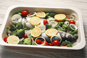 Raw fish with vegetables and lemon in baking dish on wooden table