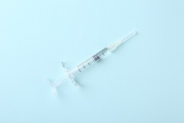 Injection cosmetology. One medical syringe on light blue background, top view