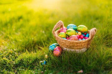 Fototapeta na wymiar Easter eggs in basket in grass. Colorful decorated easter eggs in wicker basket. Traditional egg hunt for spring holidays. Morning magical light