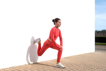 sporty woman doing leg stretching exercises outside against a white wall