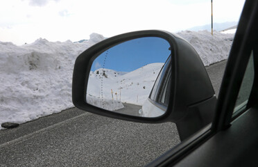 Rearview mirror of the passenger car on the mountain road in winter with snow and reflection
