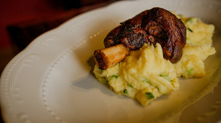 Succulent Baked Lamb Shank Served Atop Creamy Mashed Potatoes on a White Plate