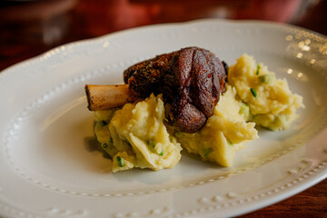 A savory baked lamb shank resting on a bed of creamy mashed potatoes, ready for dining.