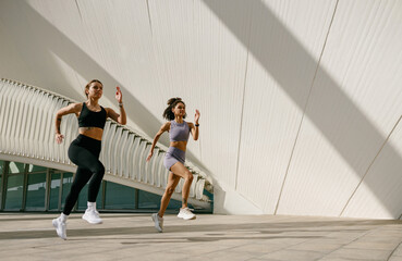 Active women athlete running side by side along an outdoor track on modern buildings background