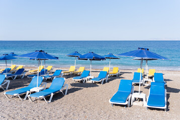 View of beach in the resort town of Rhodes in Greece covered with parasols and sunbeds of vibrant...