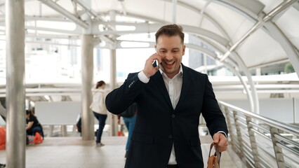 Smart caucasian businessman calling his colleague to plan financial strategy while walking to workplace. Front view of manager using mobile phone to communicate with marketing team. Lifestyle. Urbane.