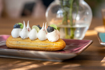 Handmade eclairs are displayed on a ceramic plate standing on a wooden table. eclair with white...