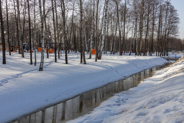 Thaw in the city park, snow melting, accumulated water in the ditch. spring flood, sunny day in the park.