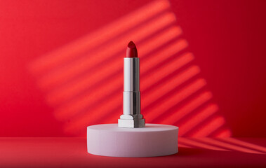 Elegant red lipstick on a white block with a cool red background.
