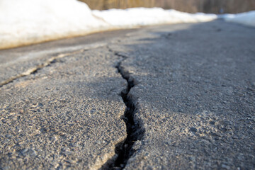 Close-up of cracks in the asphalt pavement, sidewalk in perspective, damage to the road surface in the spring, snow melting on the treadmill