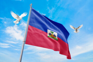 Waving flag of Haiti in beautiful sky and flying pigeons. Haiti flag for independence day. The symbol of the state on wavy fabric.