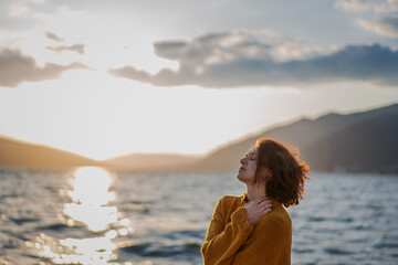 Smiling young woman in a yellow sweater looking at view at sunset enjoy sunshine. - 761733393