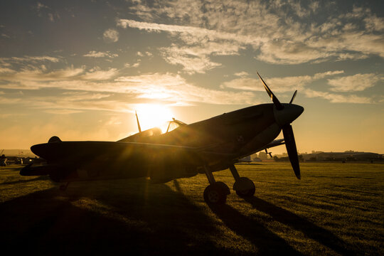 The sun rises behind a Spitfire at an airshow and shines through the cockpit glass.