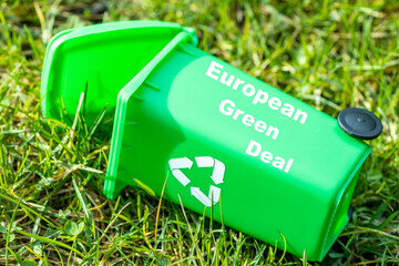 green garbage bin lying in the grass with the text European Green Deal, Environmental concept, Changes in the Green Deal, Farmers' protests, ecological project