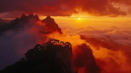 Foto op Aluminium Fiery sun dips behind cloud-covered peaks - A stunning landscape image shows the sun setting behind lofty mountain ridges with fiery skies and clouds in a dramatic display © Mickey