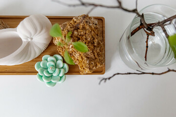 Easter concept. Shell rock, cactus, candle, tree branch with green leaves in a glass vase. White table, light background. Wooden plate. Ceramic seashell.